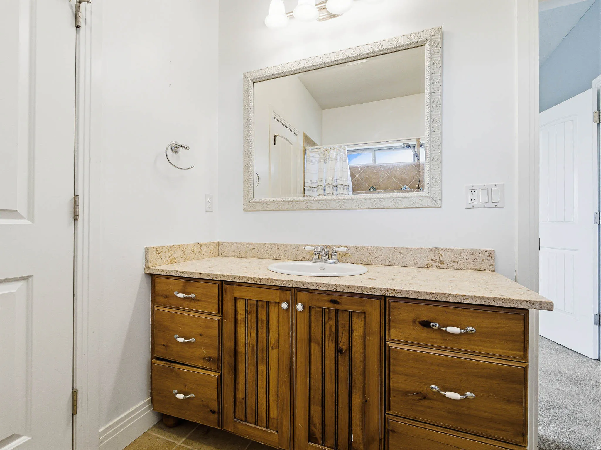 Vanity featuring a light-toned countertop with integrated sink, wood cabinetry, and a framed mirror