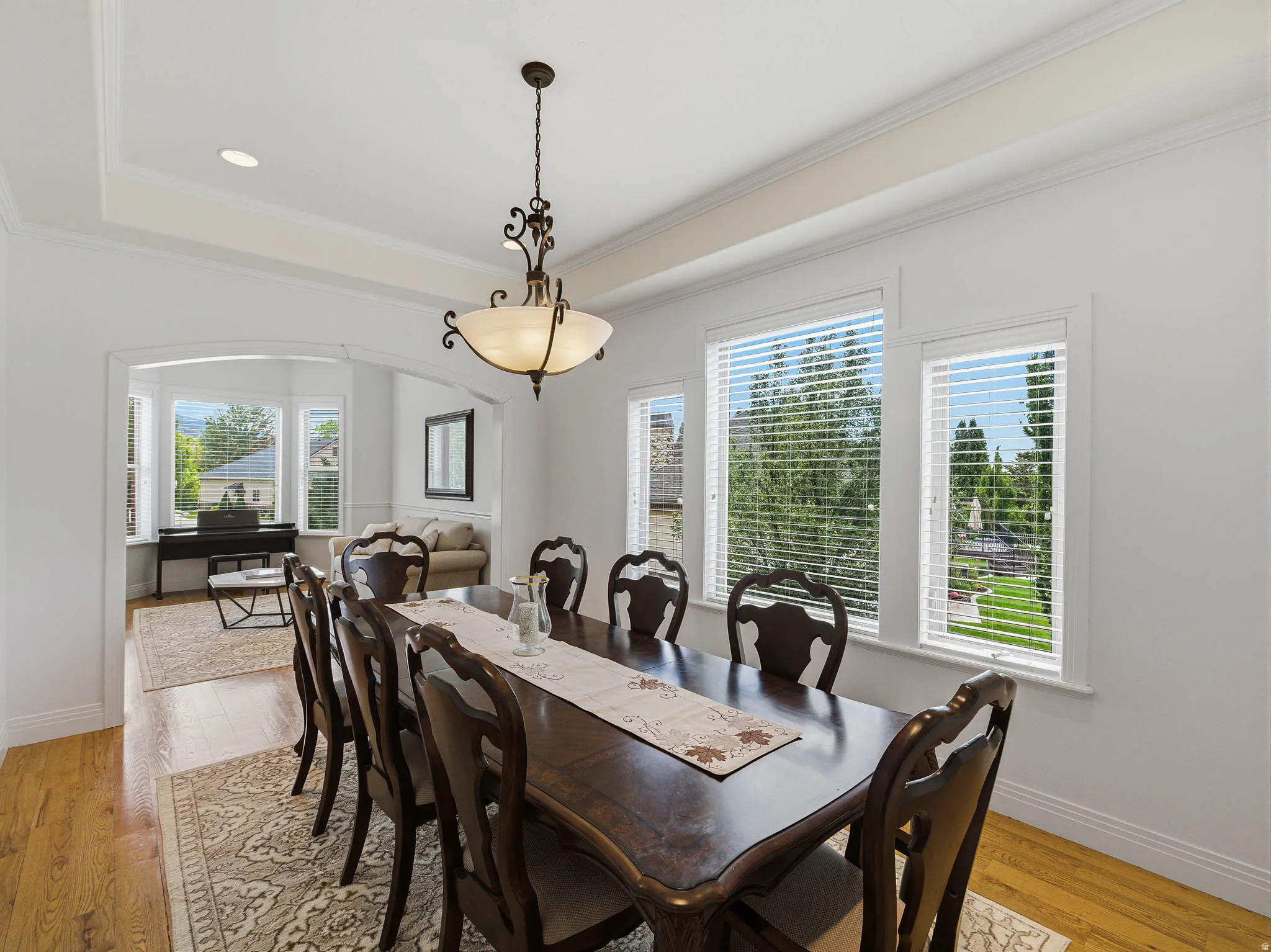 Dining area featuring tray ceiling with recessed lighting, central chandelier, and three large windows
