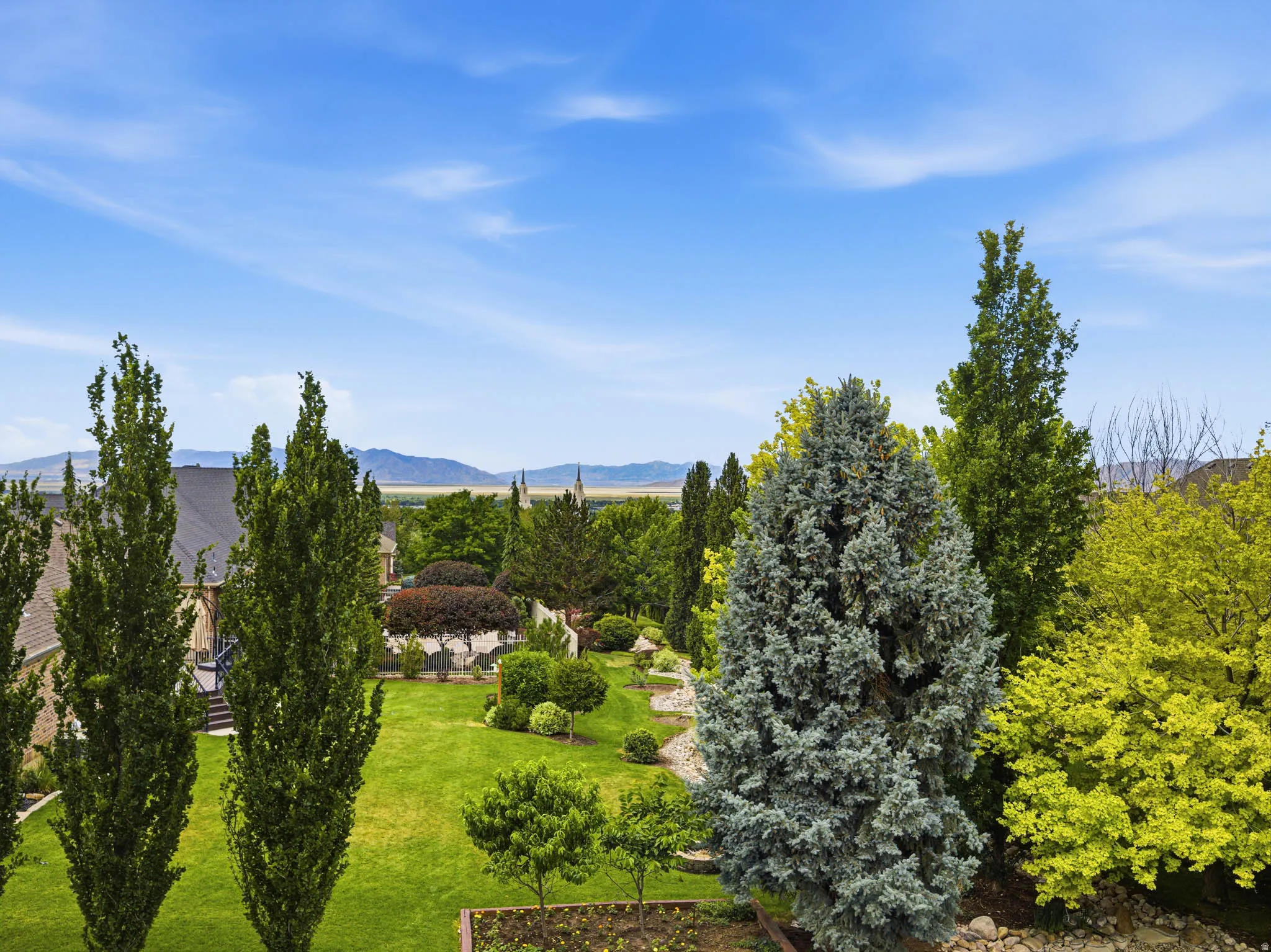 Expansive rear yard featuring a large lawn, diverse mature trees, and landscaping with stone accents