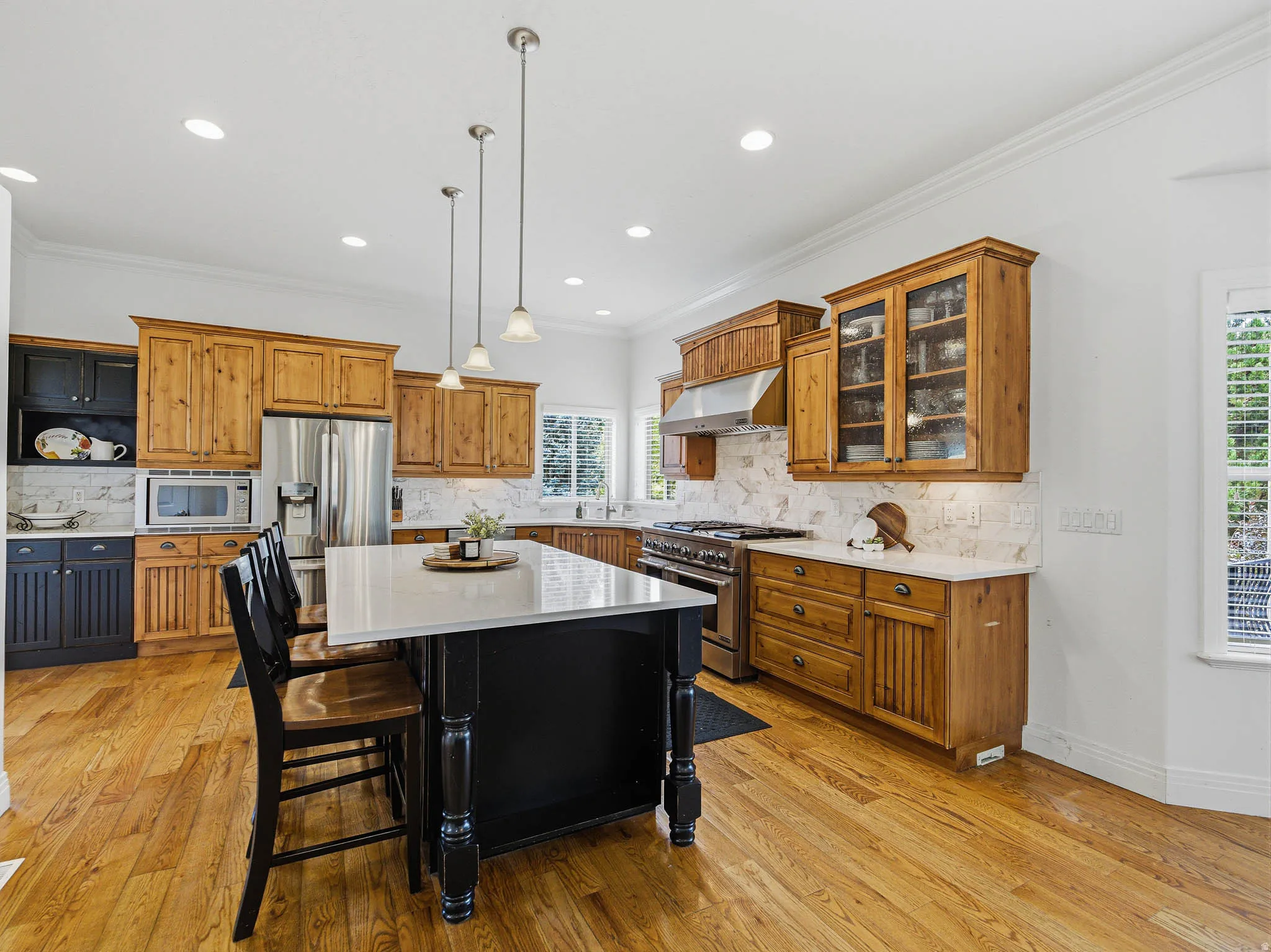 Spacious kitchen featuring a central island with seating, natural wood cabinetry, a stainless steel range with hood, stone-finish backsplash, and wood-finish flooring