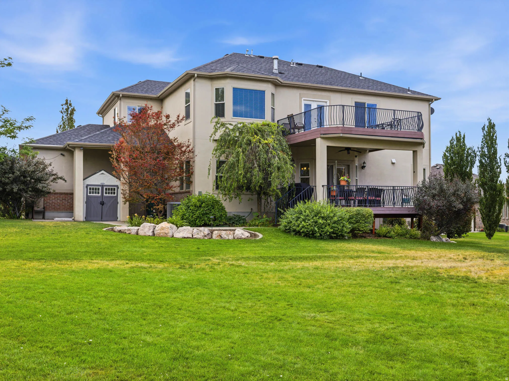 Expansive green lawn bordering a two-story stucco exterior with a multi-level deck