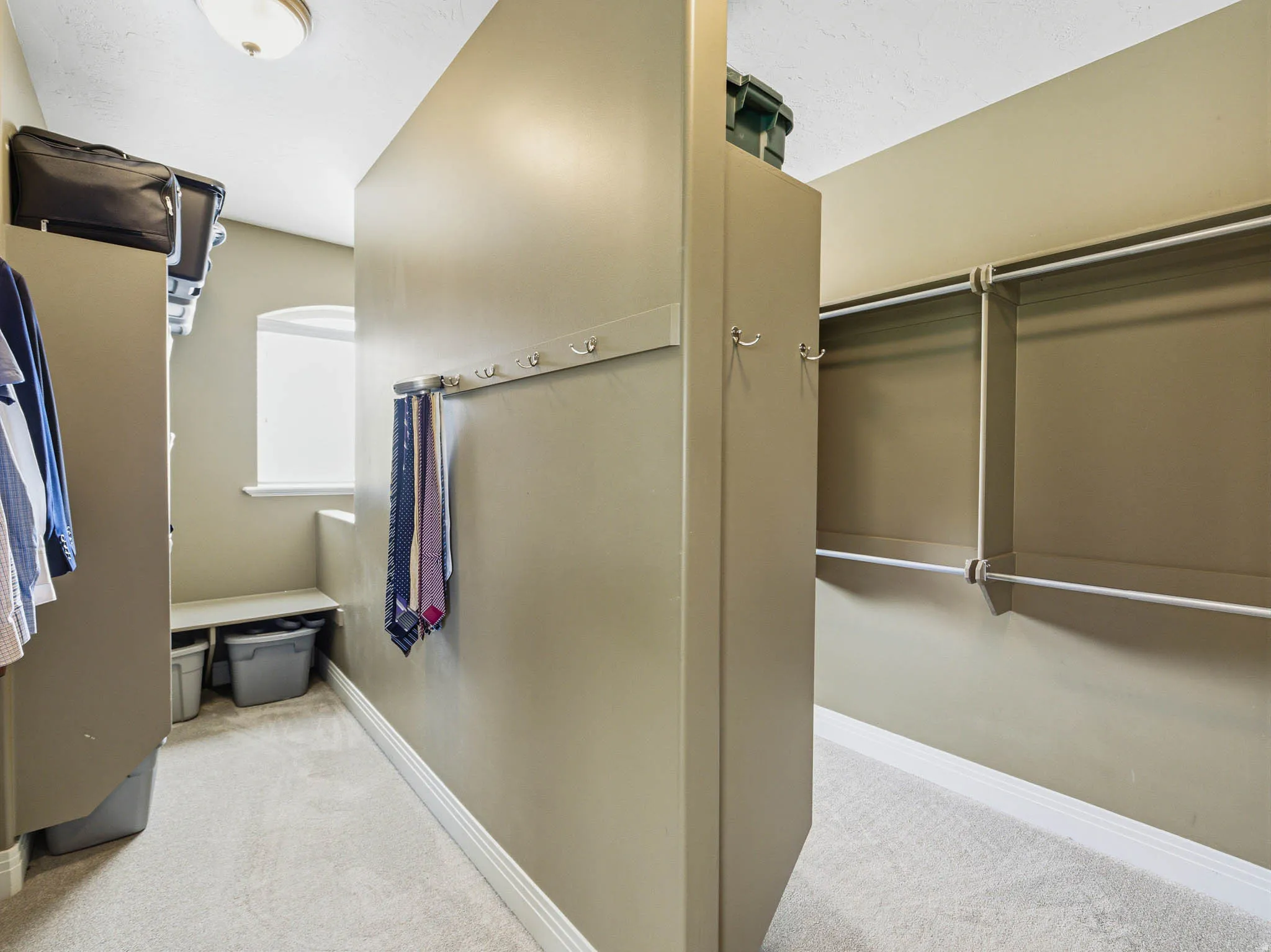 Spacious walk-in closet featuring light beige wall paint, plush carpeting, a built-in window bench, and an integrated hanging rod system