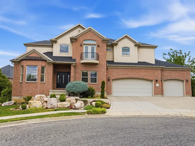 Brick and stucco exterior residence featuring a prominent bay window, upper-level balcony, and a dual-door entry