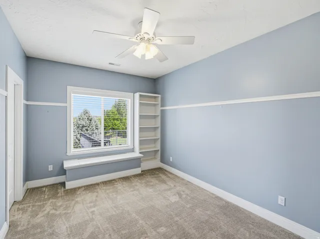 Carpeted room featuring a large window with blinds, a window seat, and built-in shelving
