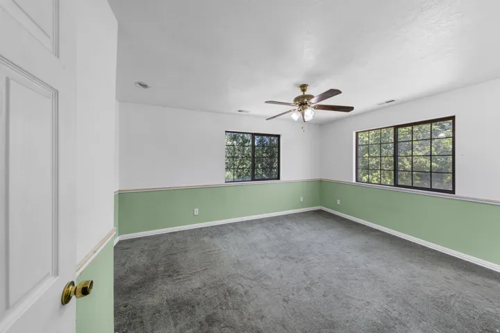 Spacious room featuring multiple large windows with black grilles, a brass-finish ceiling fan with integrated lighting, and carpet flooring