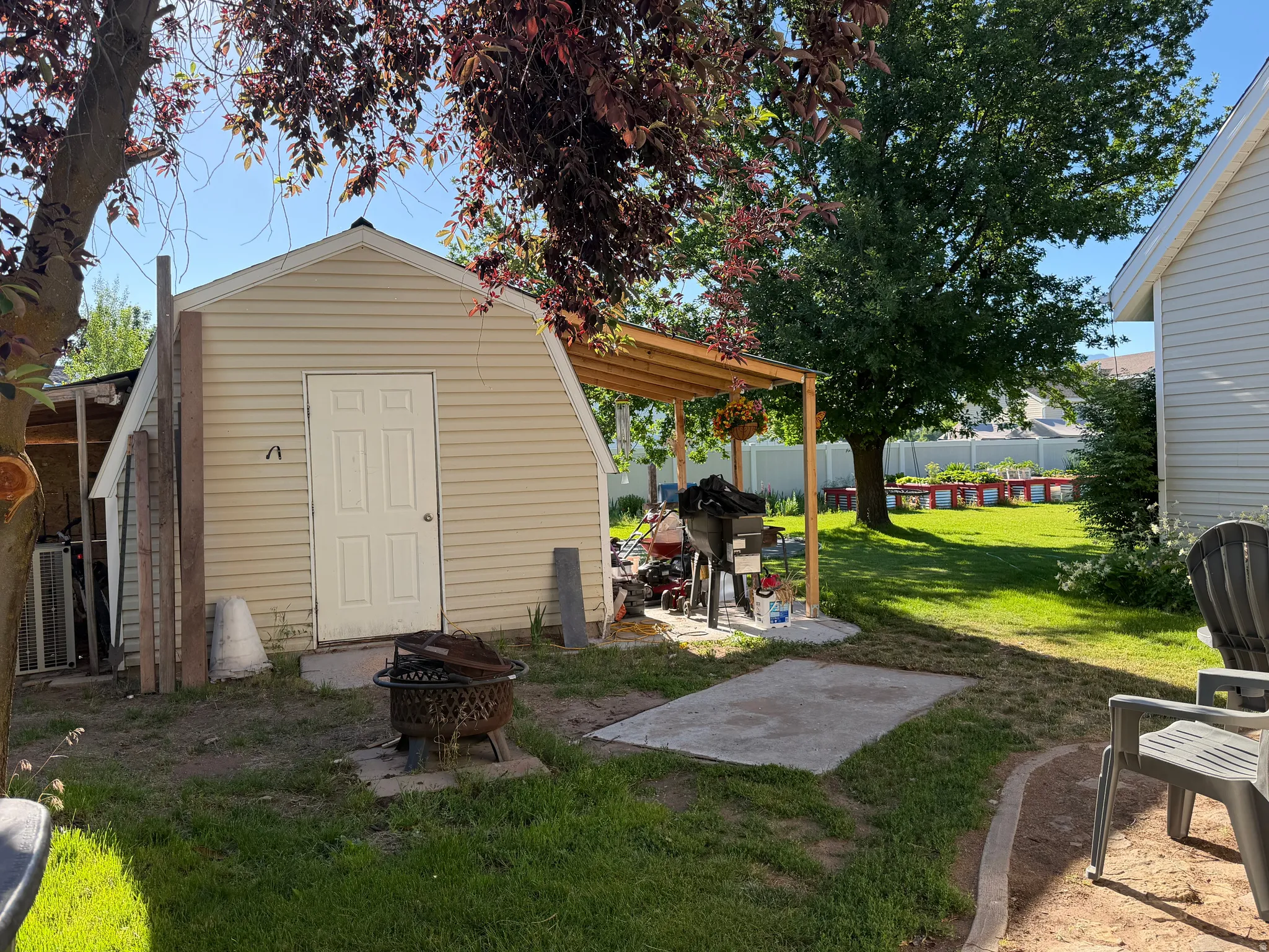 Detached utility shed with vinyl siding and a gable roof, featuring an attached wooden pergola