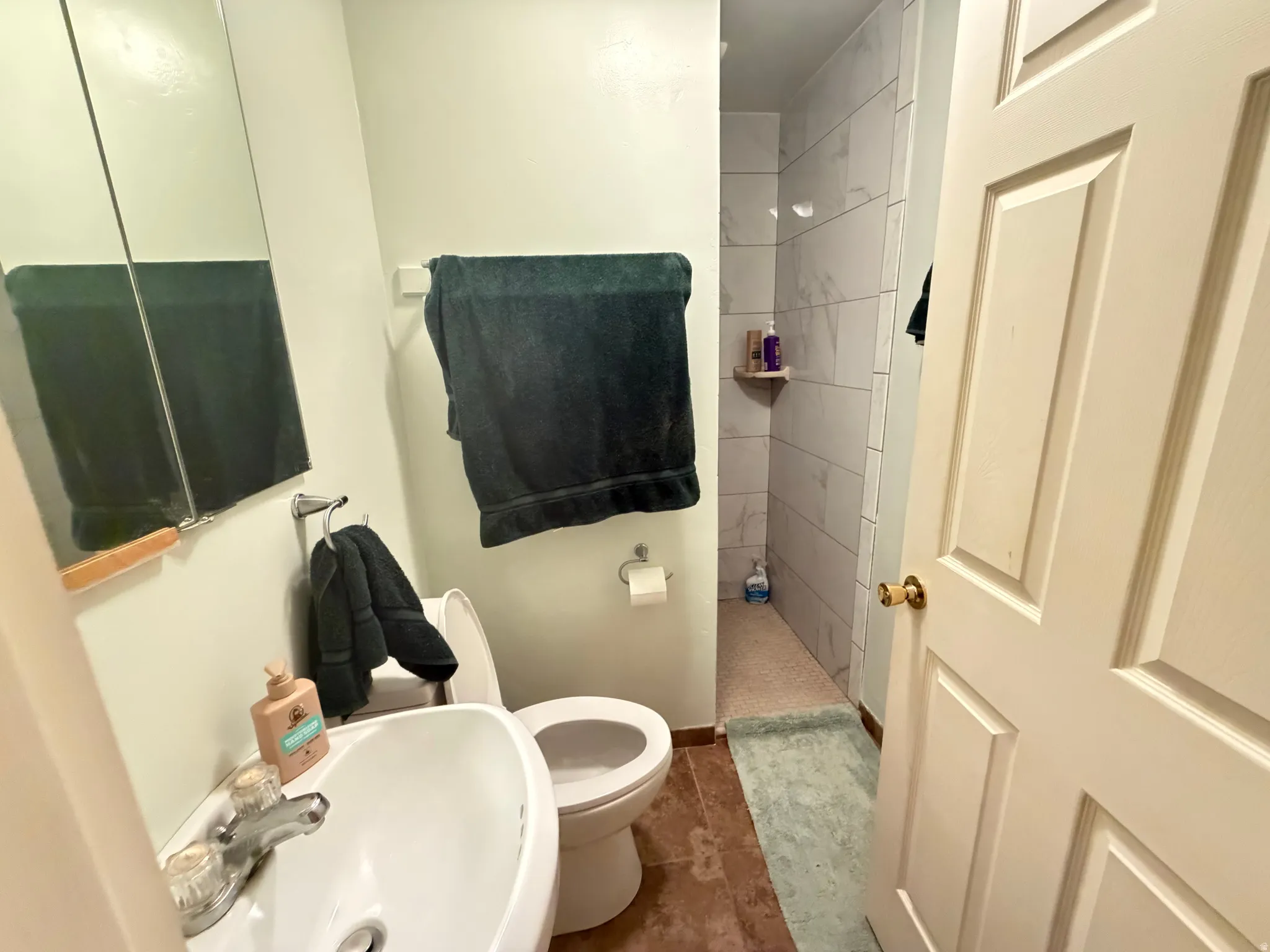 Bathroom featuring a single vanity, wall-mounted mirror, commode, and a shower with light-toned tile surround