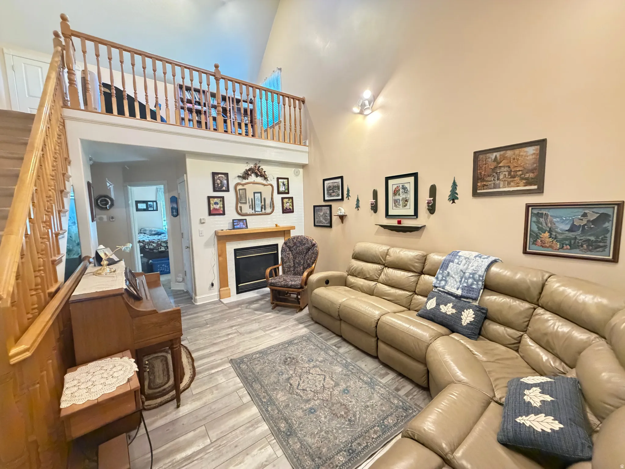 Living area with vaulted ceilings featuring wood-finish flooring, a fireplace with a wood mantel, and a staircase leading to a loft space with a wood railing