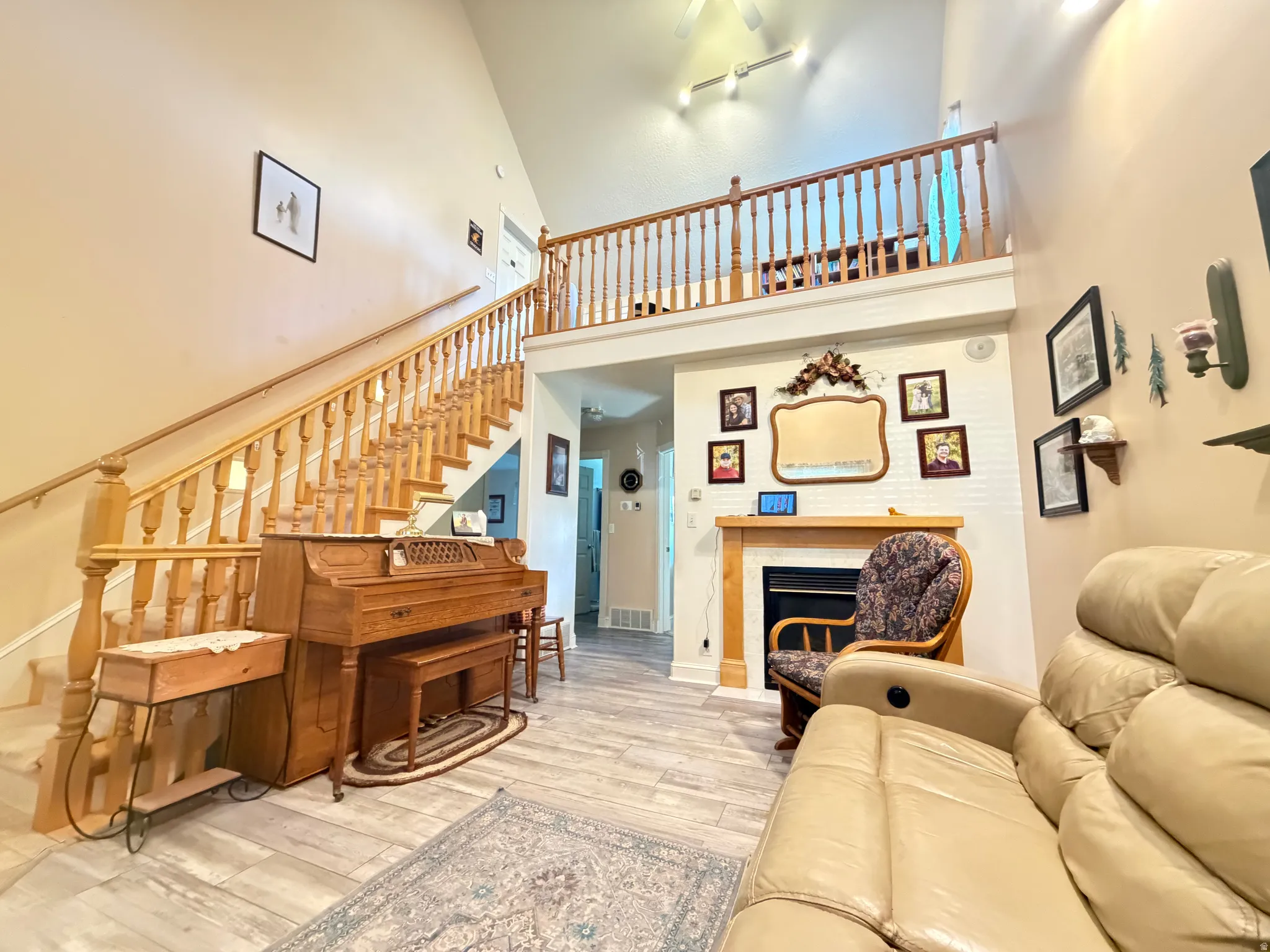 Living area with vaulted ceilings, wood-finish flooring, a prominent wooden staircase with balusters, a built-in fireplace with a white brick surround and wood mantel, and an upper-level balcony with a matching wooden railing