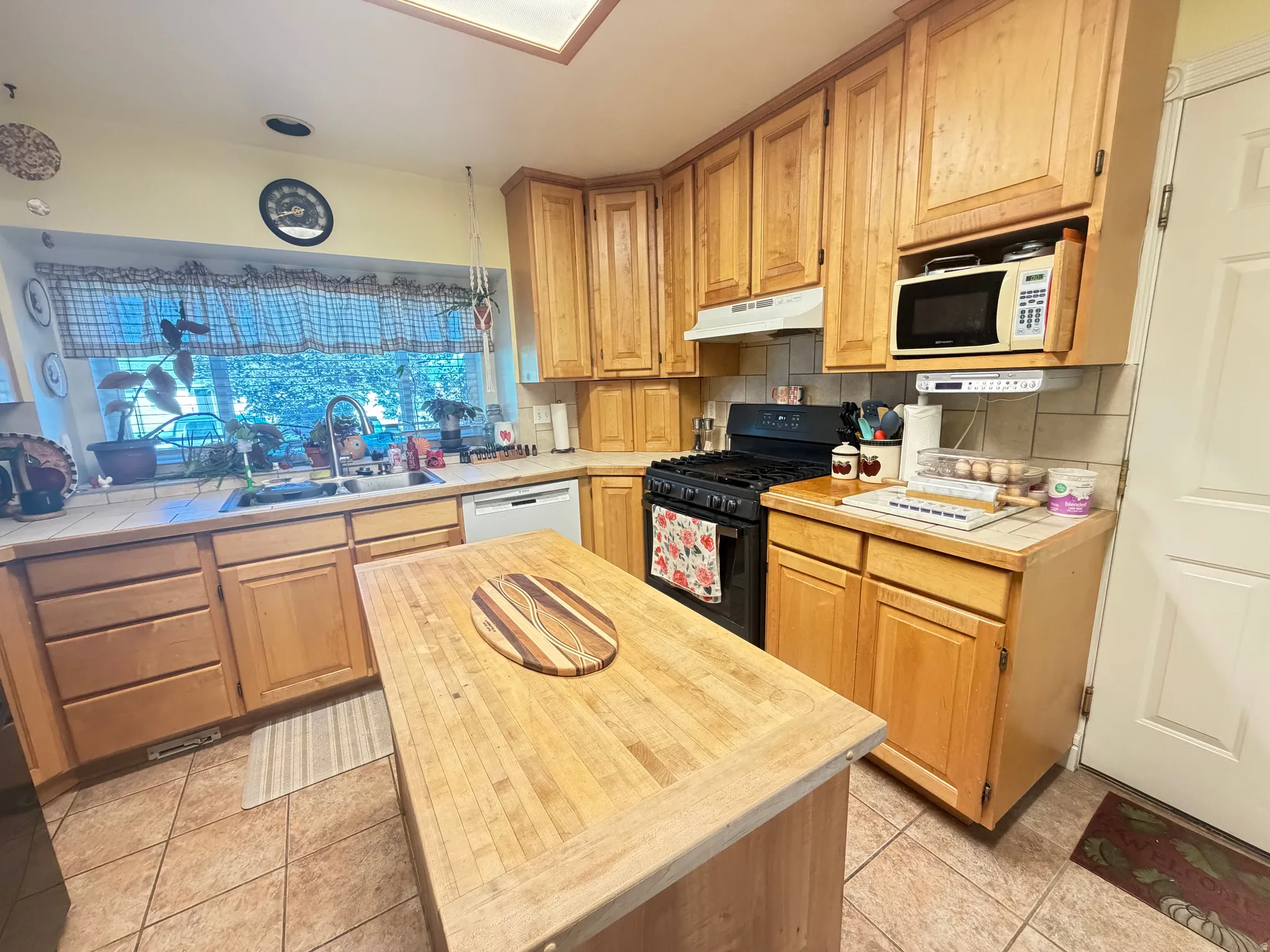 Kitchen featuring extensive natural wood cabinetry, tile flooring, a gas range, a built-in microwave, and a substantial island with a butcher block top