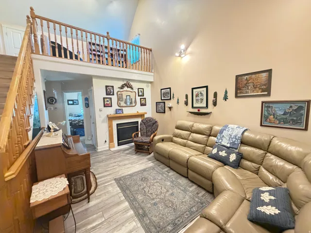 Living area with vaulted ceilings featuring wood-finish flooring, a fireplace with a wood mantel, and a staircase leading to a loft space with a wood railing