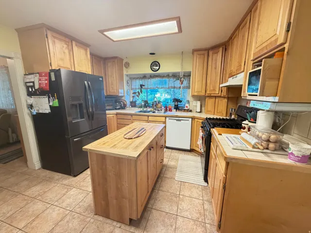 Kitchen featuring abundant wood cabinetry, a central island with a wood-finish countertop, tiled flooring, a gas range, and a window above the sink