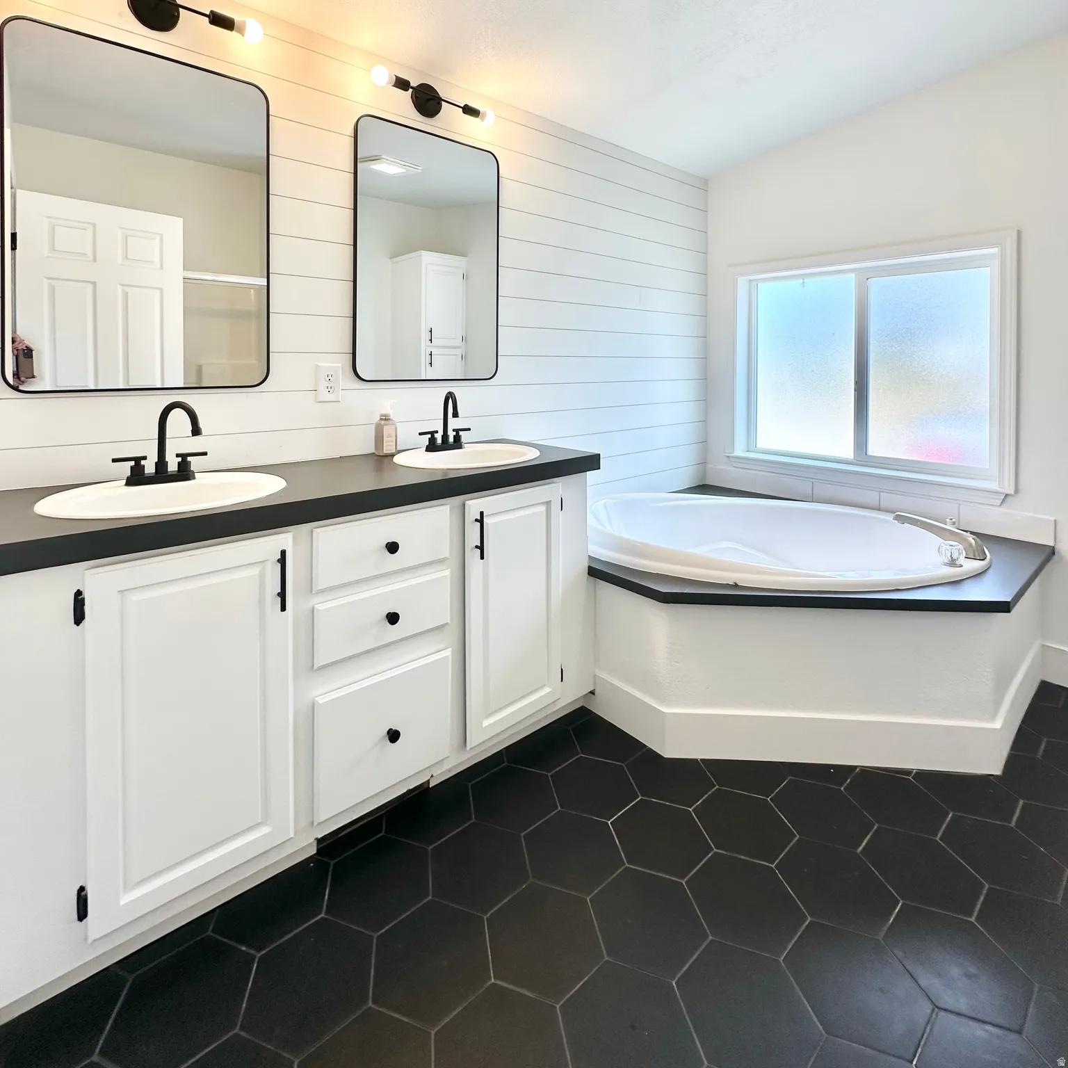 Bathroom featuring dual vanities with white cabinetry and dark countertops
