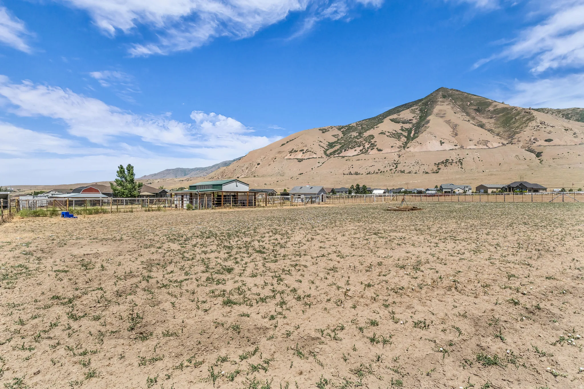 Expansive open lot with a mountain backdrop, perimeter fencing, and distant structures including a barn with a green roof