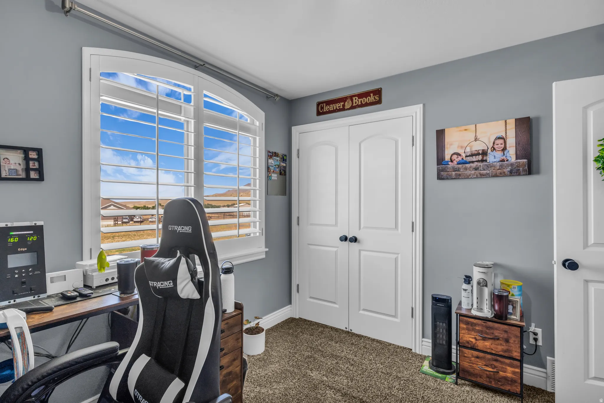 bedroom currently used as an office with arched window with plantation shutters, featuring a distant landscape