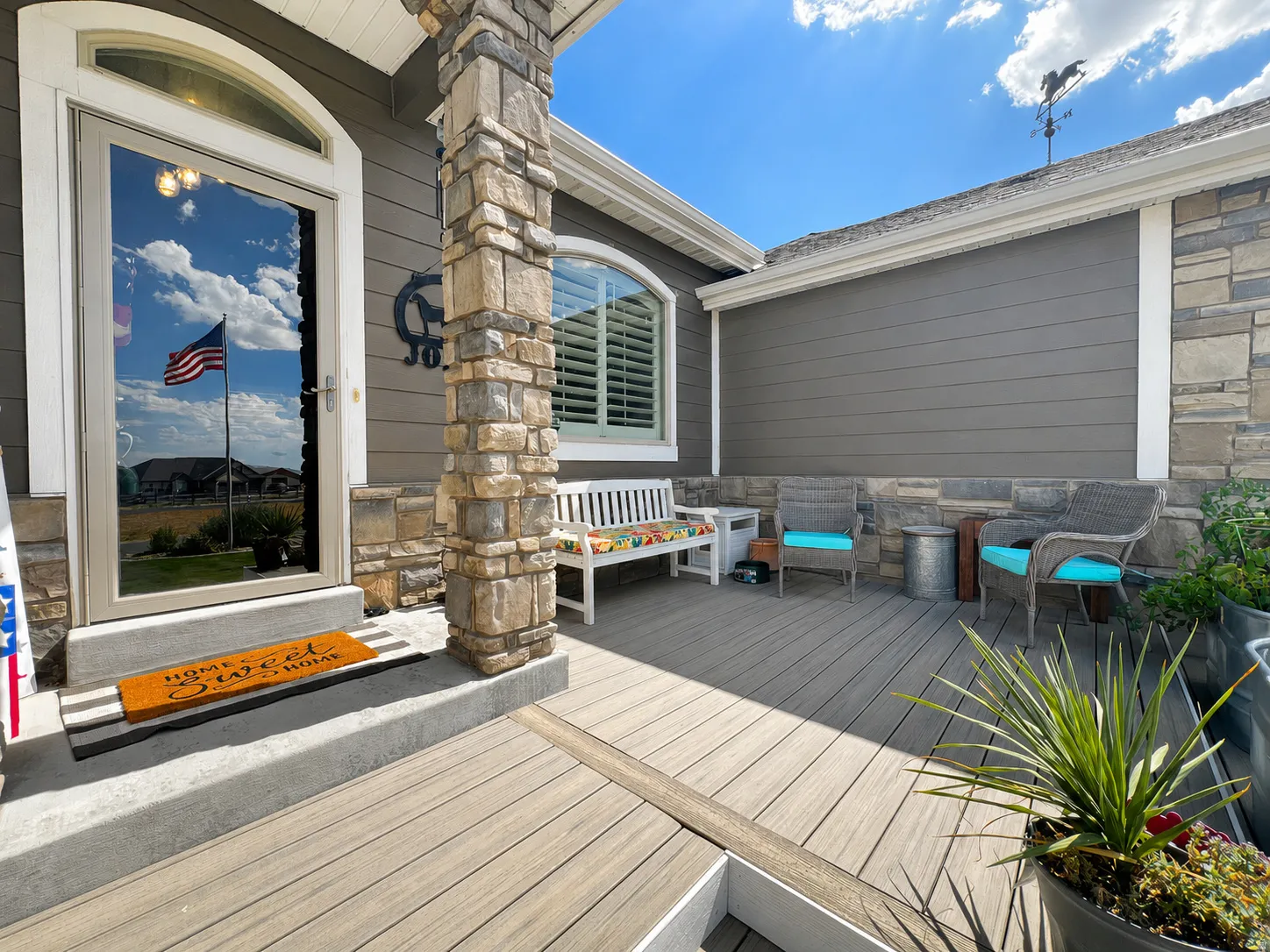 Inviting front porch featuring stone-clad pillars, gray horizontal siding, and a spacious composite decking surface