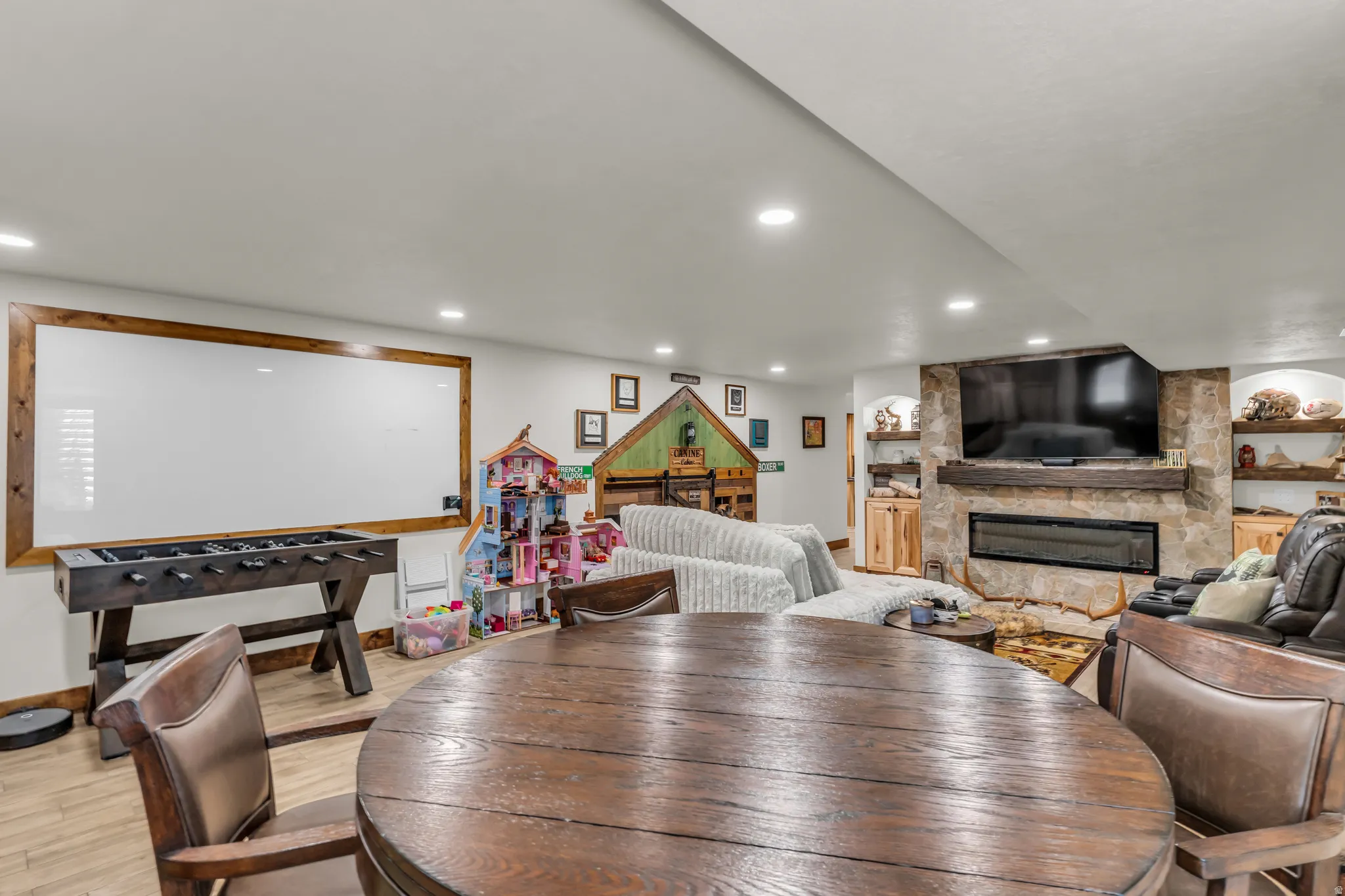 Spacious recreation room featuring wood-finish flooring, recessed lighting, and a stone-clad fireplace with a wood mantel