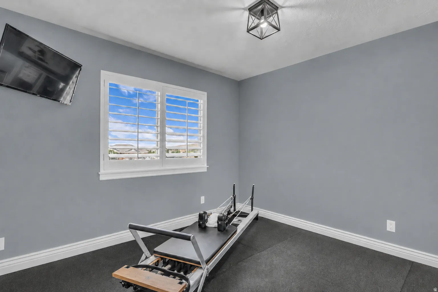 Room featuring a window with white plantation shutters, gray walls, and dark flooring