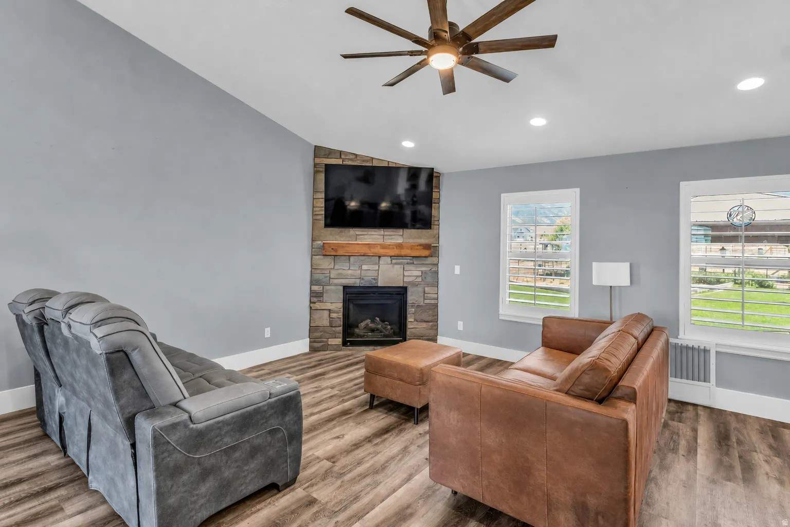 Living area featuring a floor-to-ceiling stone fireplace with a wood mantle, wood-finish flooring, vaulted ceiling, and recessed lighting