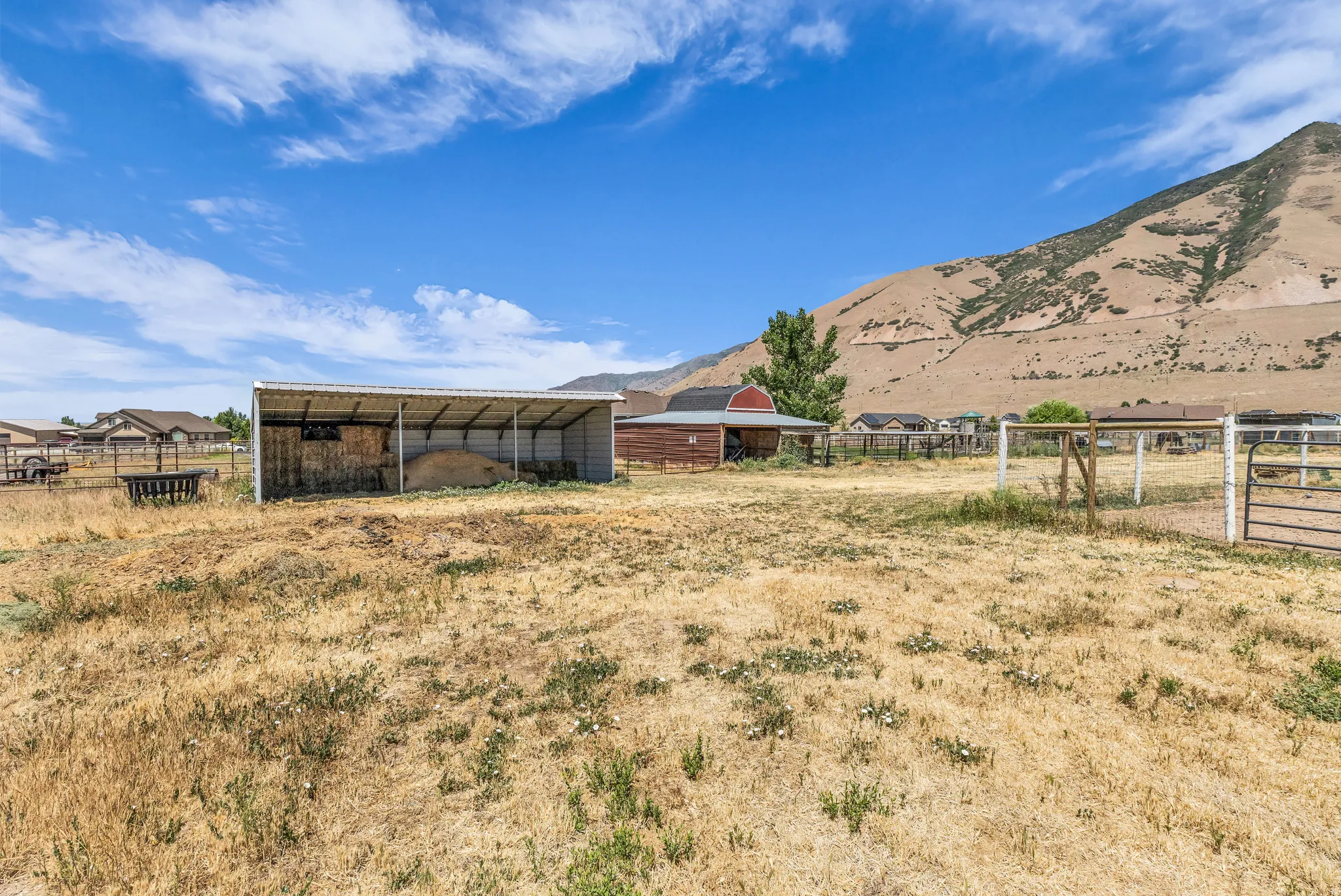 Expansive open land featuring a metal-roofed shelter, a red barn structure, and mountain scenery
