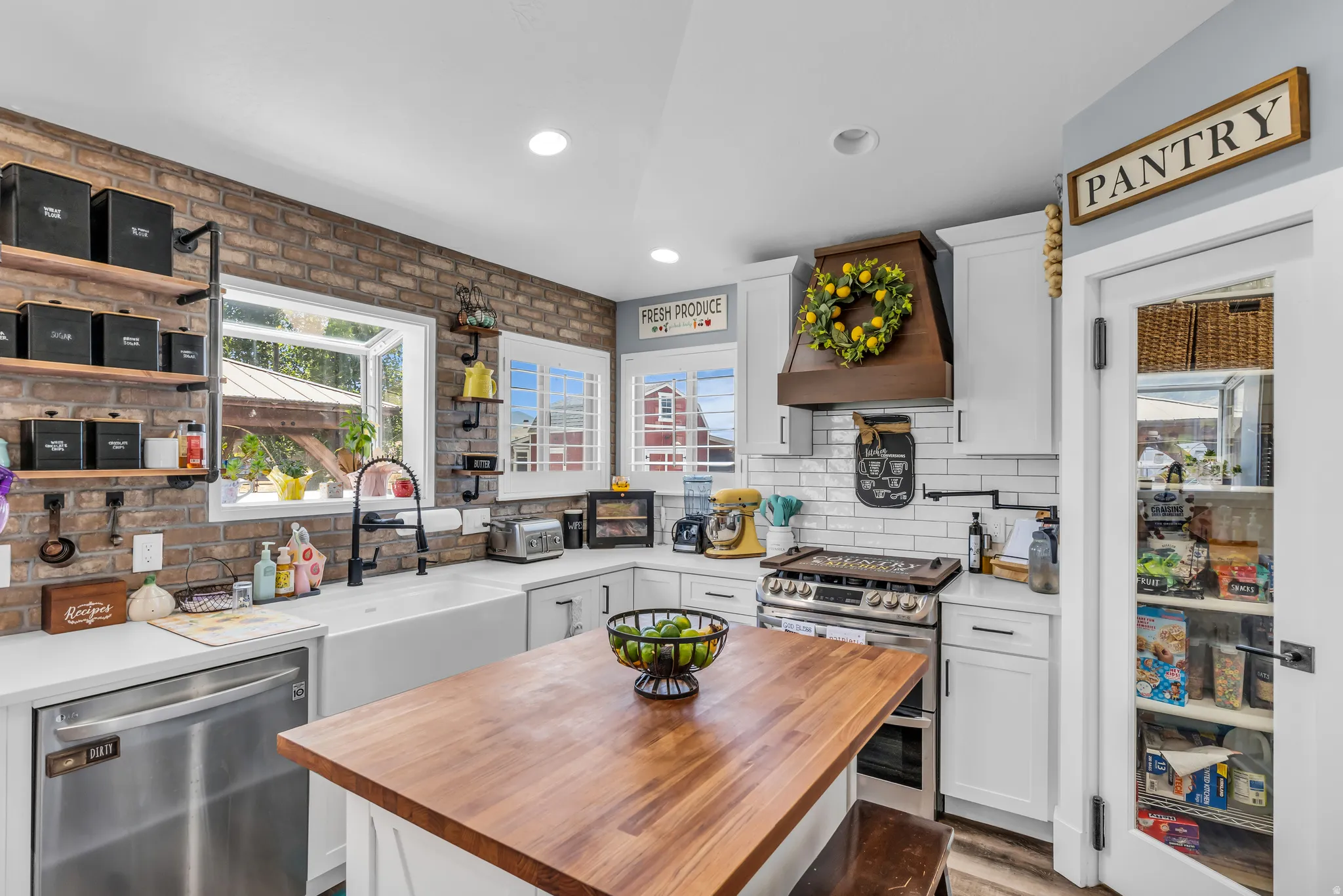 Kitchen featuring a central wood-finish island, white cabinetry, stainless steel appliances, a farmhouse sink, and a glass-paneled pantry door