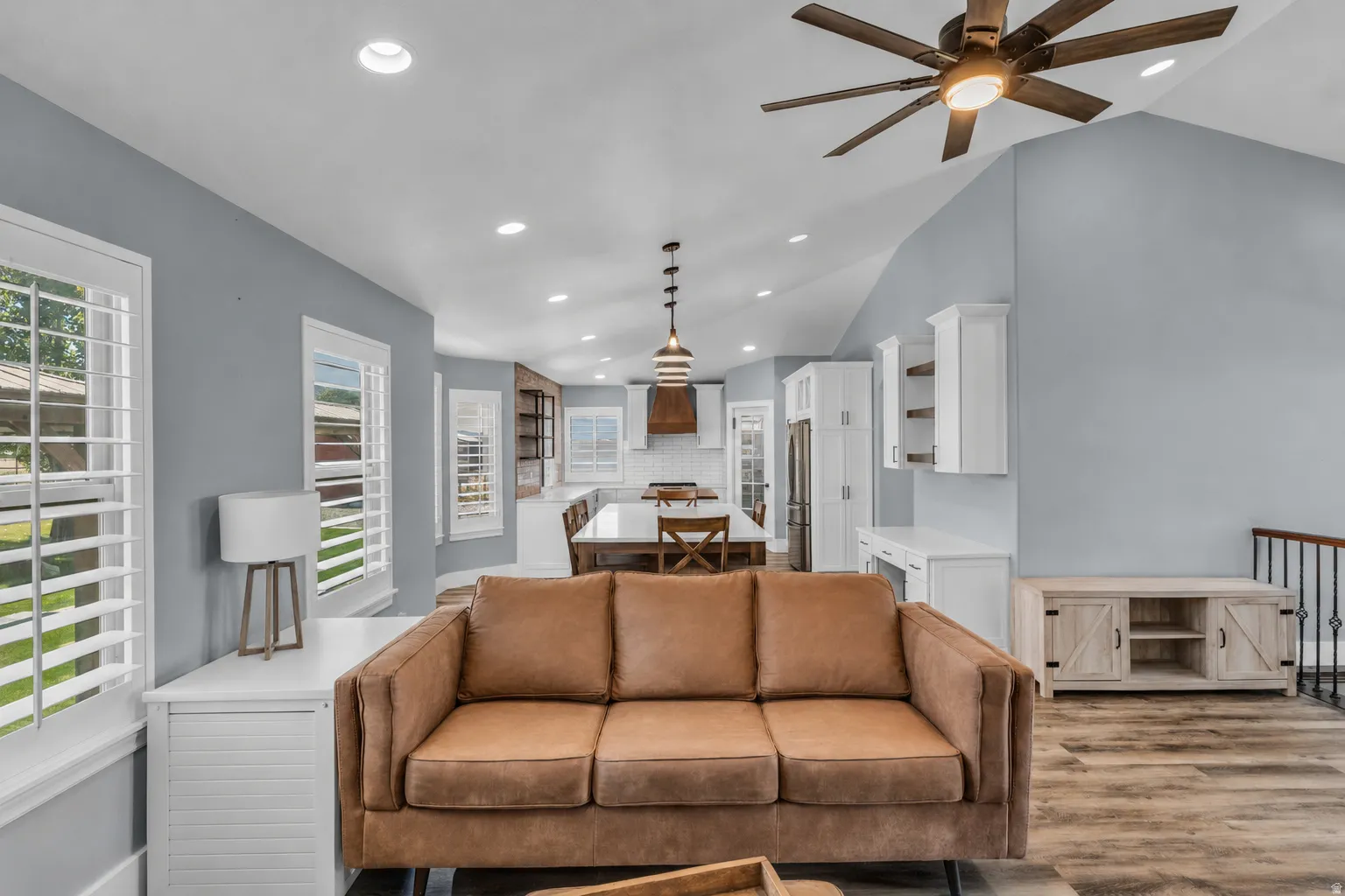 Open-concept living area with vaulted ceilings, recessed lighting, wood-finish flooring, and white plantation shutters