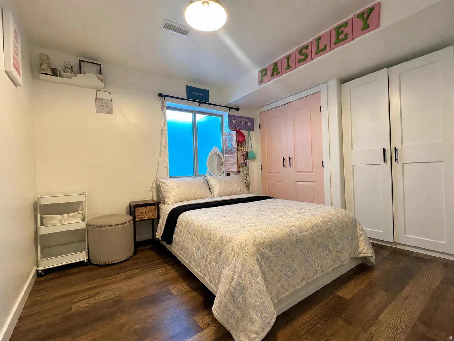 Room featuring wood-finish flooring, two sets of white paneled closet doors with black hardware, and a window with privacy film