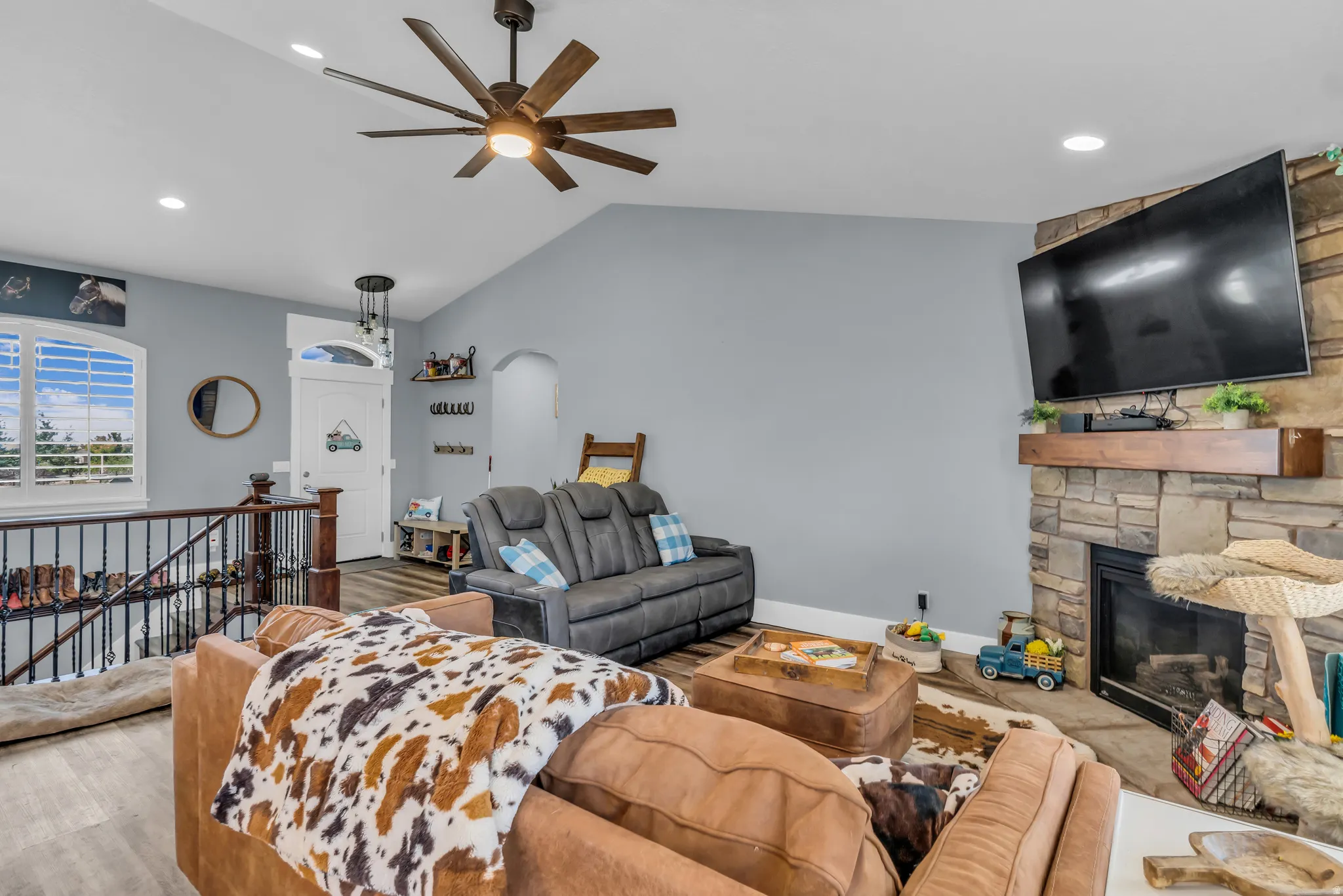 Spacious living area featuring vaulted ceilings, wood-finish flooring, a stone-front fireplace with a wood mantle, and a ceiling fan