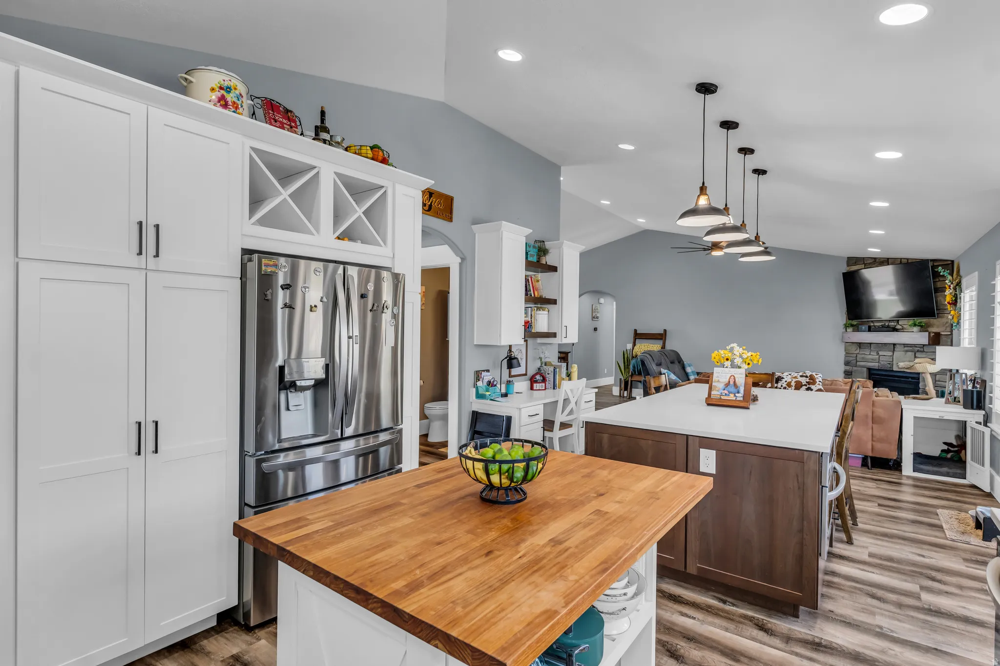 Open-concept kitchen featuring white shaker cabinetry, an integrated stainless steel refrigerator, and a wood-finish island countertop