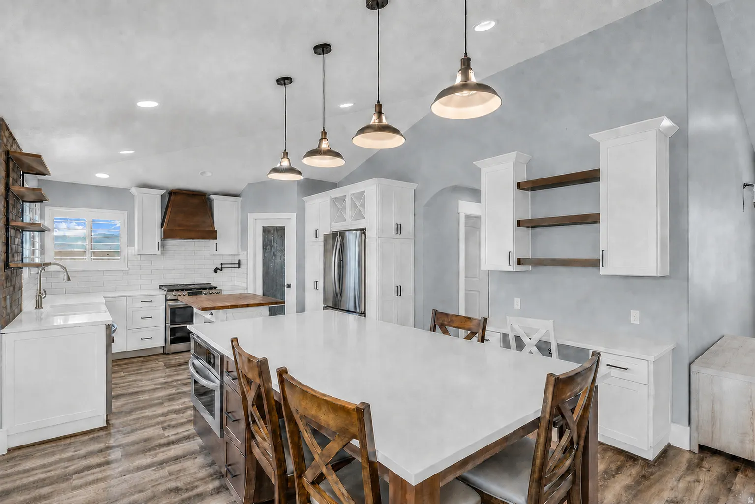 Kitchen featuring a large central island with seating, pendant lighting, stainless steel appliances, wood-finish flooring, and white cabinetry