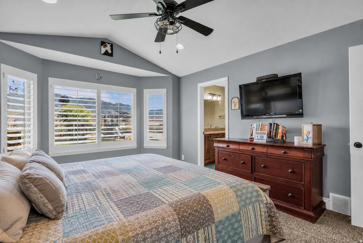 Bedroom featuring a vaulted ceiling, ceiling fan with integrated lighting, and a bay window with plantation shutters