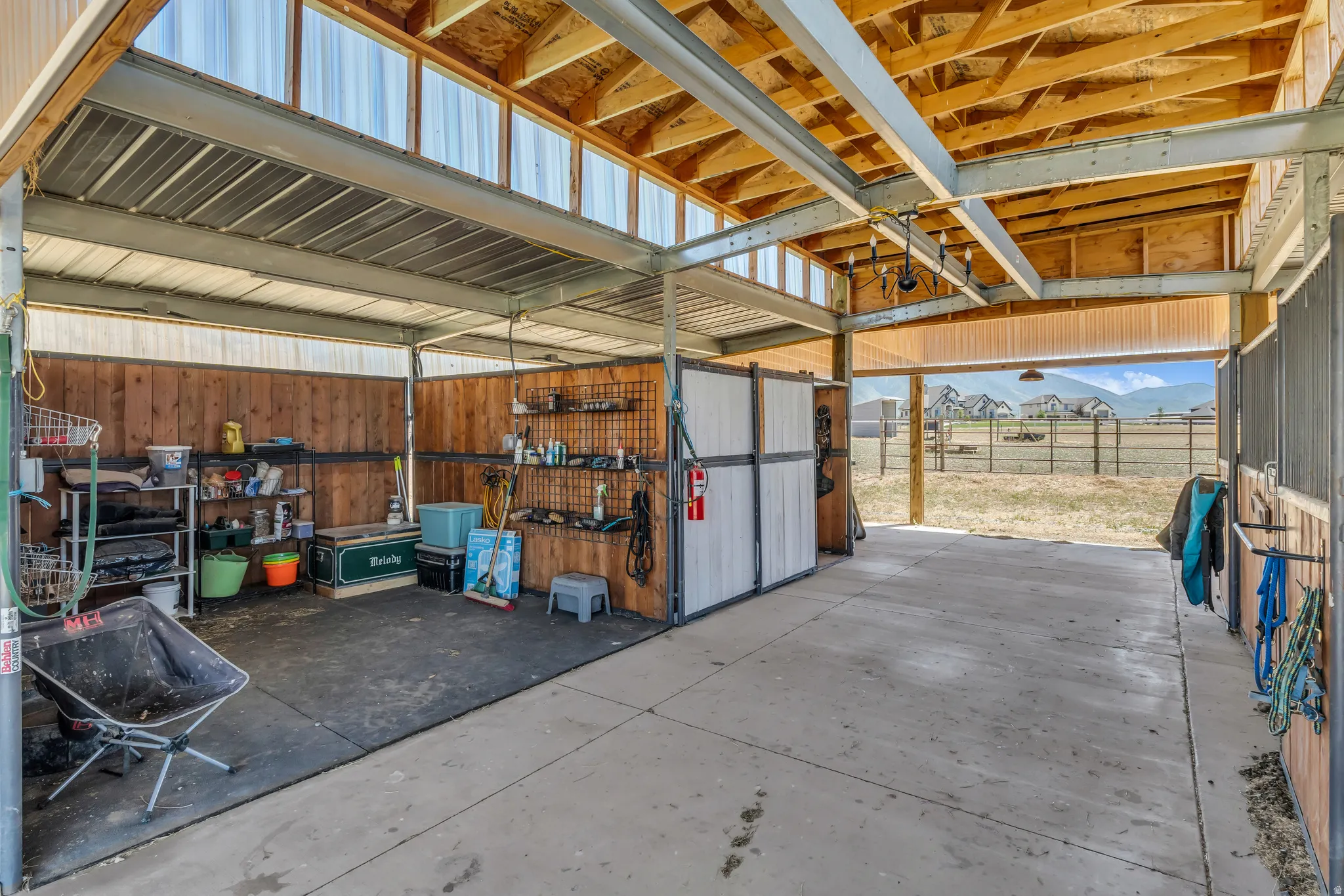 Covered outdoor structure featuring a concrete floor, wood-paneled walls, exposed wood beam ceiling, metal support beams, and translucent roof panels