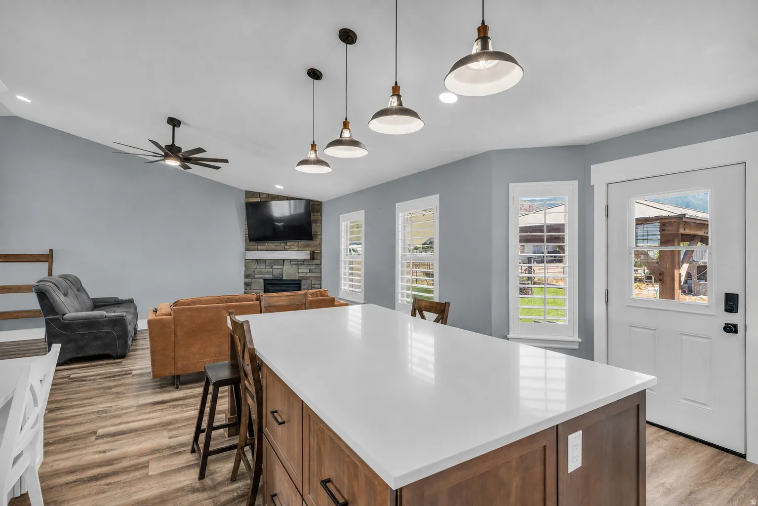 Expansive kitchen island with white countertop, dark wood-finish cabinetry, and industrial-style pendant lighting