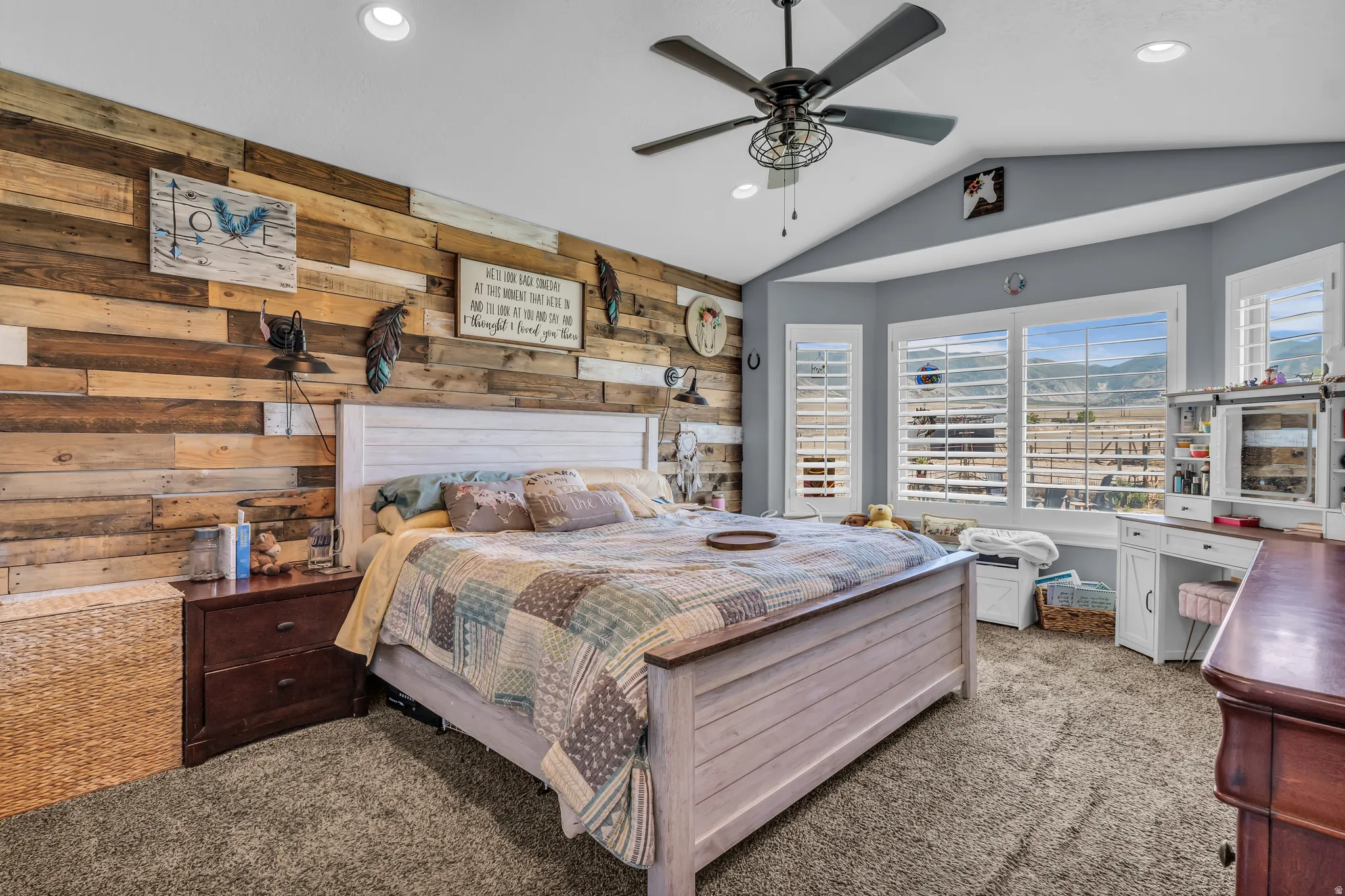 Primary Suite with vaulted ceiling room featuring a wood-panel accent wall, bay window with plantation shutters, recessed lighting, and a ceiling fan