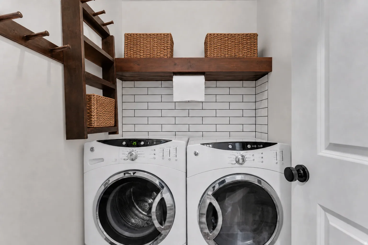 Dedicated laundry area featuring a white subway tile backsplash, a dark wood-finish floating shelf, and a dark wood-finish wall-mounted organizer