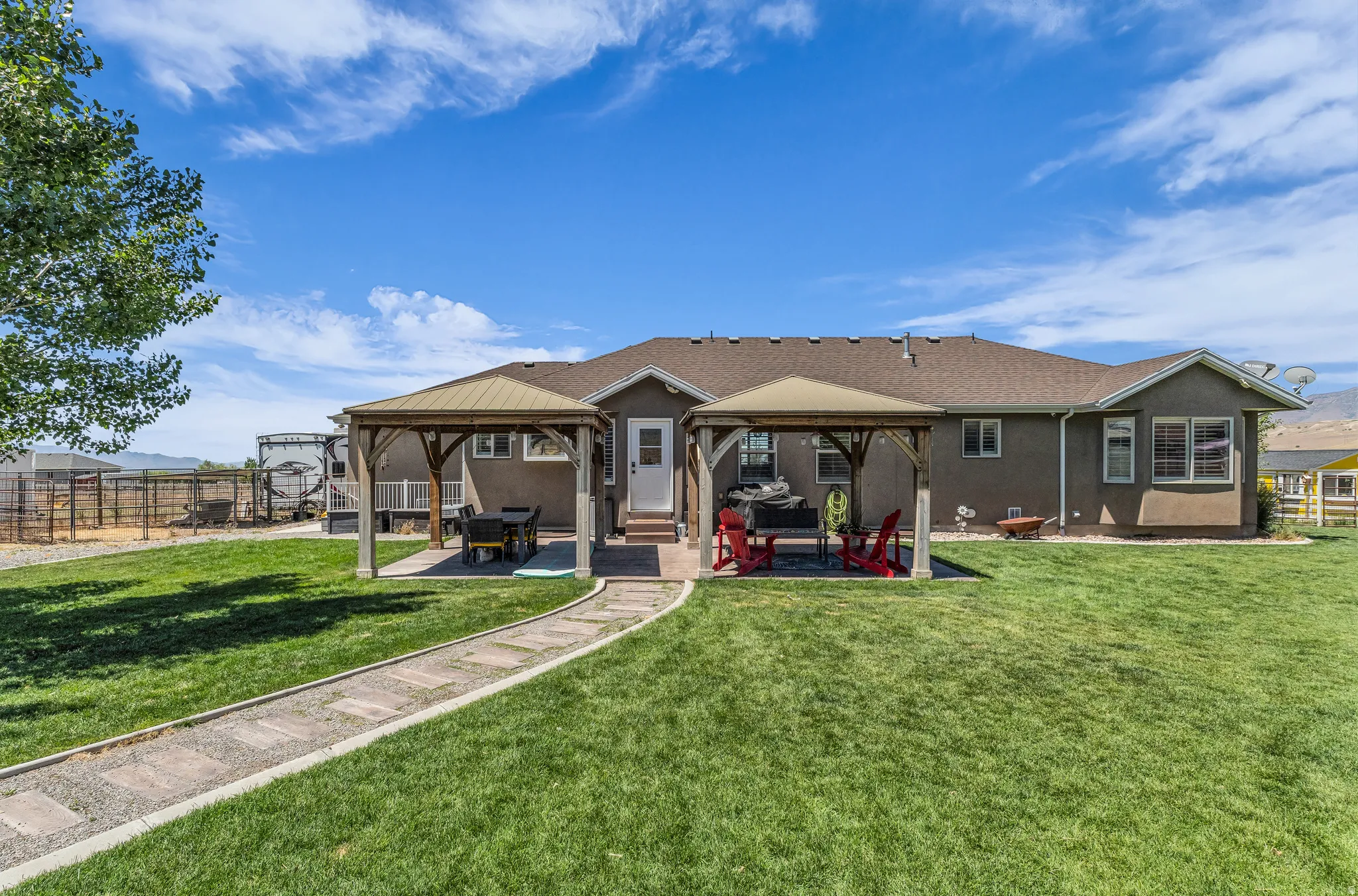 Spacious rear yard with a stone paver pathway, two permanent gazebos, and an expansive lawn area