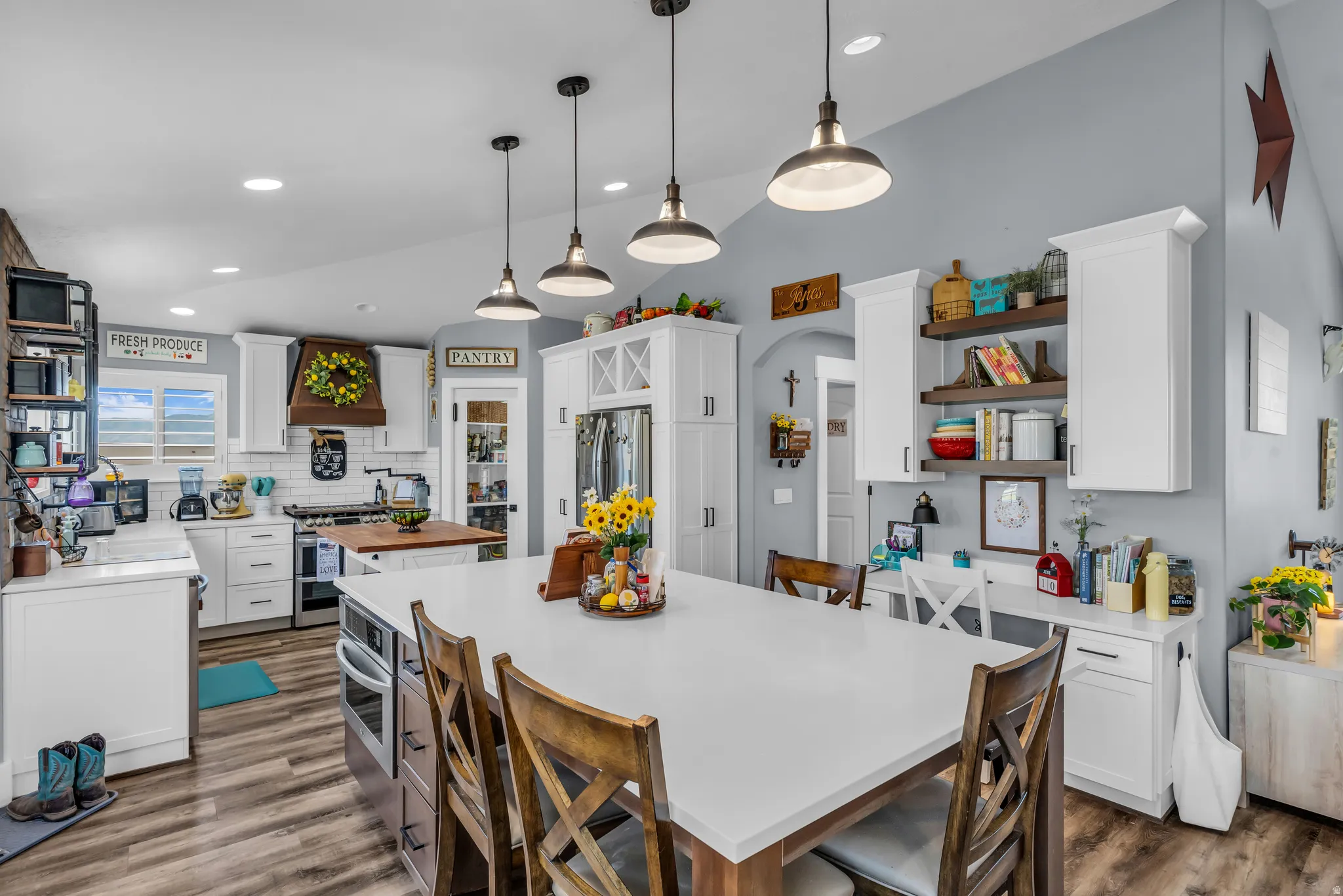 Open-concept kitchen featuring an expansive island with seating, stainless steel appliances, white cabinetry, wood-finish flooring, and a built-in desk area