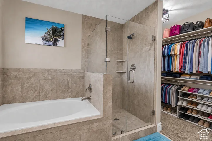 Virtually cleared of items and decor. Bathroom featuring a built-in tub with brushed nickel fixtures, a glass-enclosed shower with tile surround, and an adjacent walk-in closet with extensive custom shelving and hanging rods.