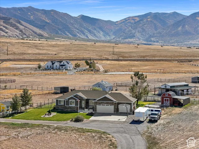 Ranch-style residence featuring a two-car garage, manicured lawn, paved driveway, and multiple outbuildings