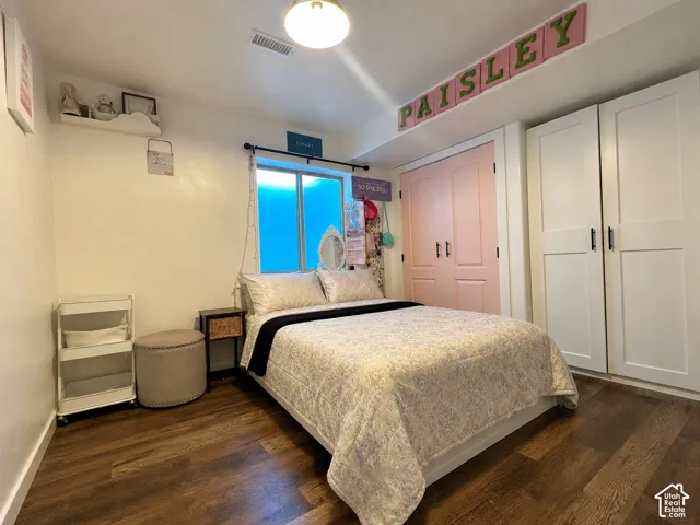 Virtually cleared of items and decor. Bedroom 5. Room featuring wood-finish flooring, two sets of white paneled closet doors with black hardware, and a window with privacy film