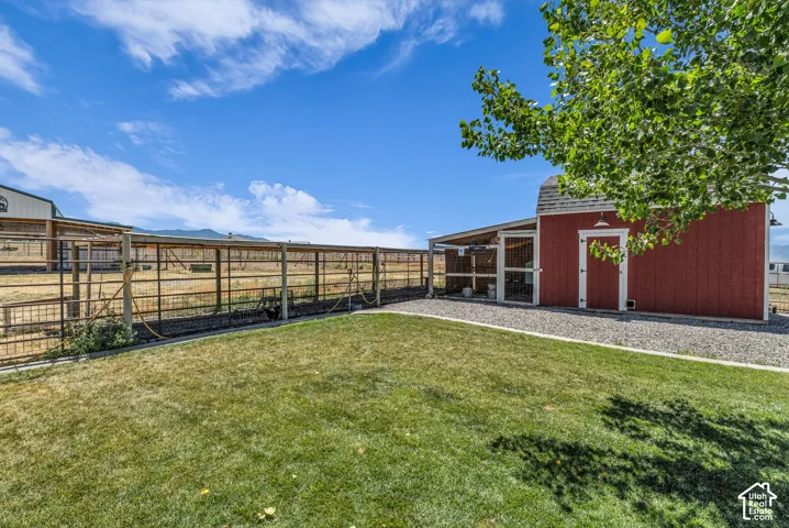Expansive grassy area featuring a red barn structure with white trim, a gravel perimeter, an attached covered enclosure, and metal fencing