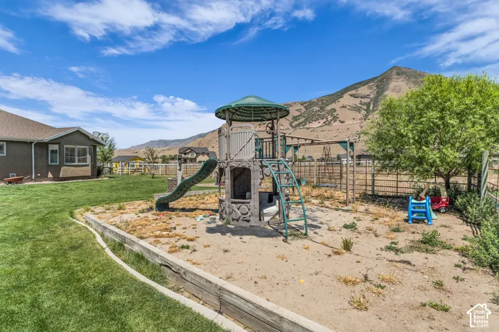 Spacious backyard featuring a large play structure, a sand-filled area, a fenced perimeter, and a distant mountainous backdrop