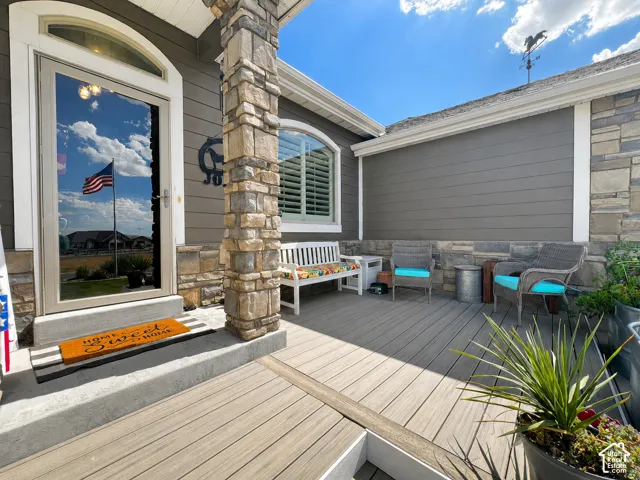 Inviting front porch featuring stone-clad pillars, gray horizontal siding, and a spacious composite deck with lots of shade