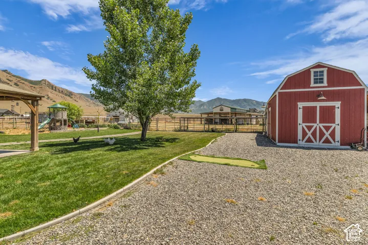 Expansive outdoor area featuring a red barn with white trim and barn doors, a gravel driveway, a manicured lawn with a mature shade tree, and a covered pergola