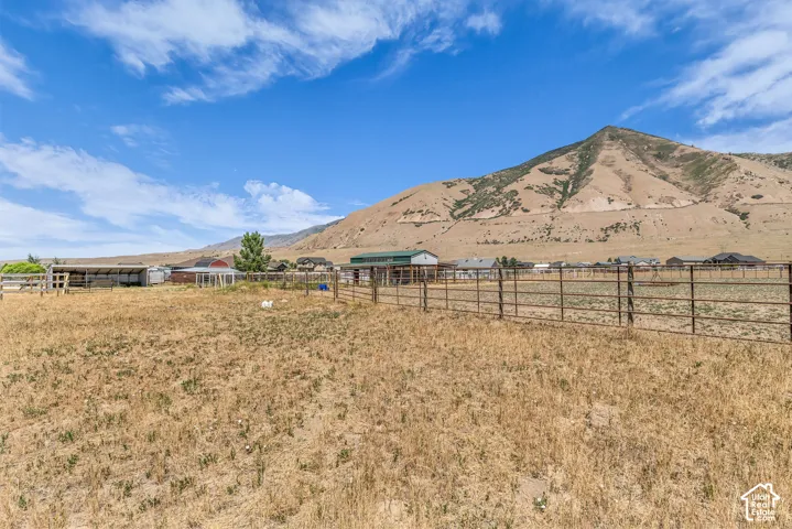 Expansive open field with perimeter fencing, featuring a barn structure, additional outbuildings, and mountain scenery