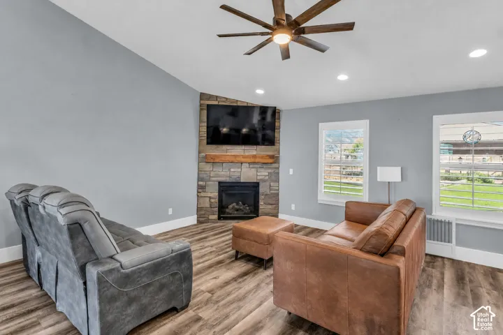 Virtually cleared of items and decor. Living area featuring a floor-to-ceiling stone fireplace with a wood mantle, wood-finish flooring, vaulted ceiling, and recessed lighting and views to the south backyard