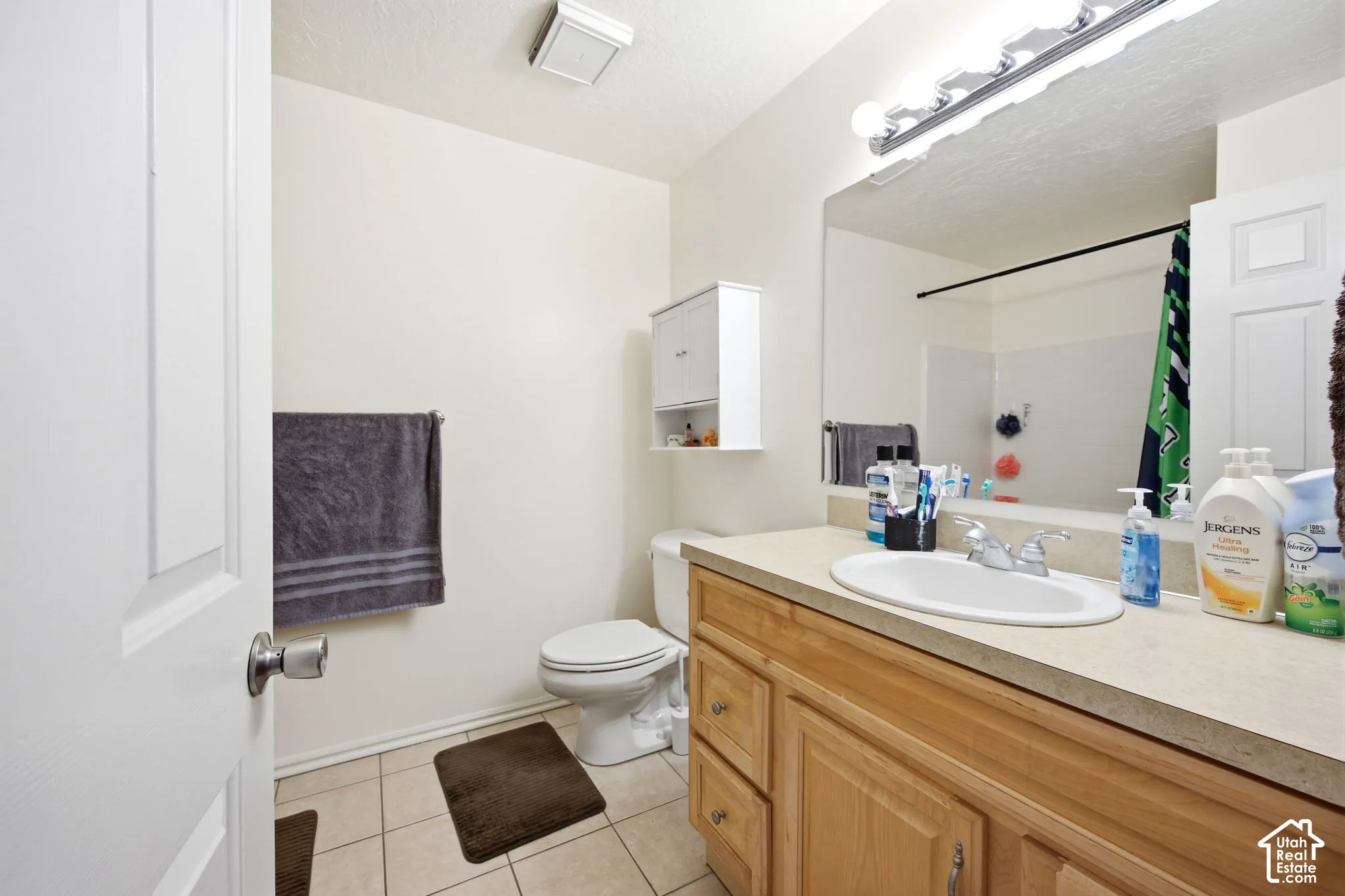 Bathroom featuring a light wood-finish vanity with an integrated sink, a large wall-mounted mirror, and tile flooring