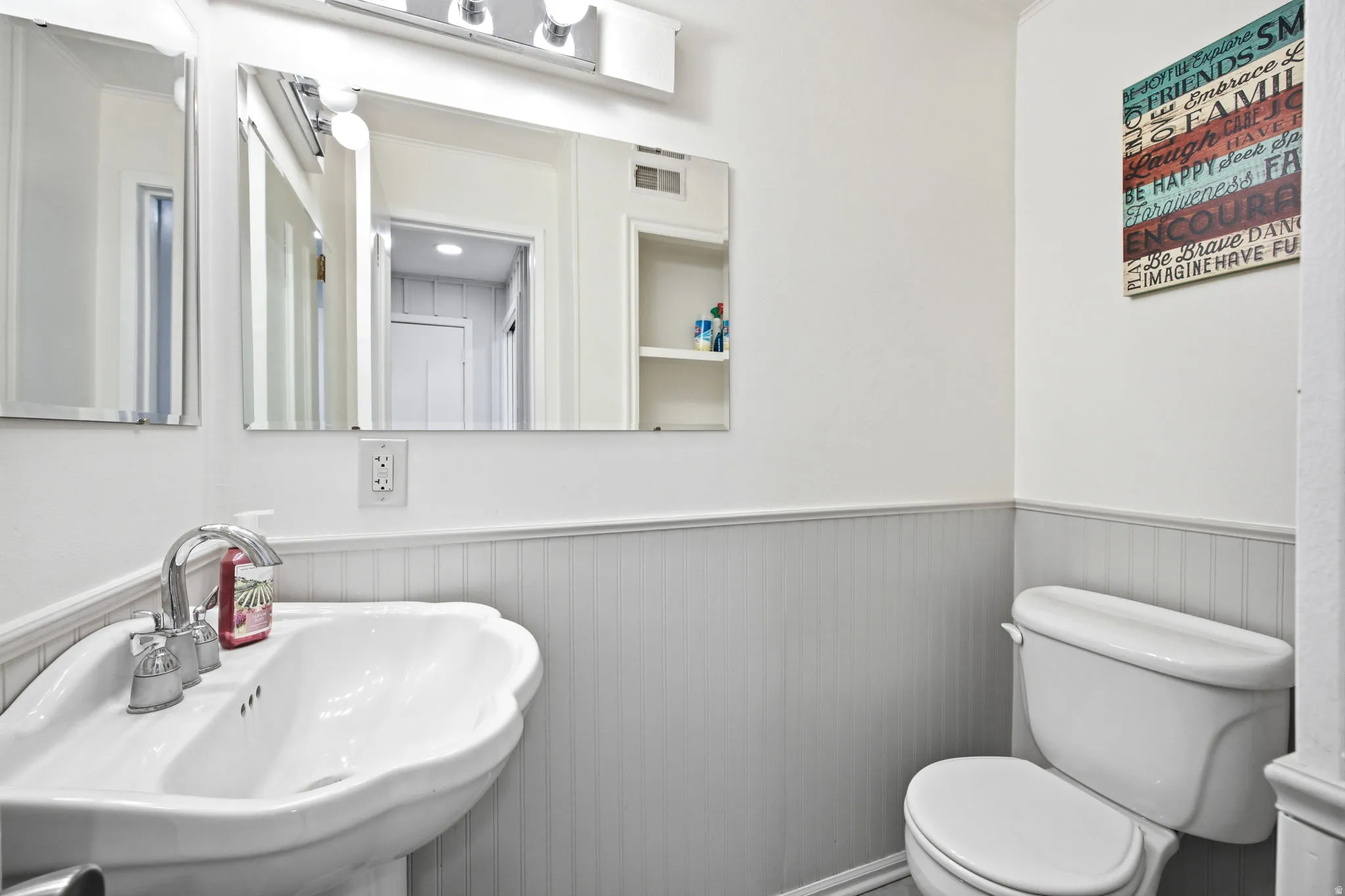 Bathroom featuring a pedestal sink with chrome faucet, a toilet, and beadboard wainscoting