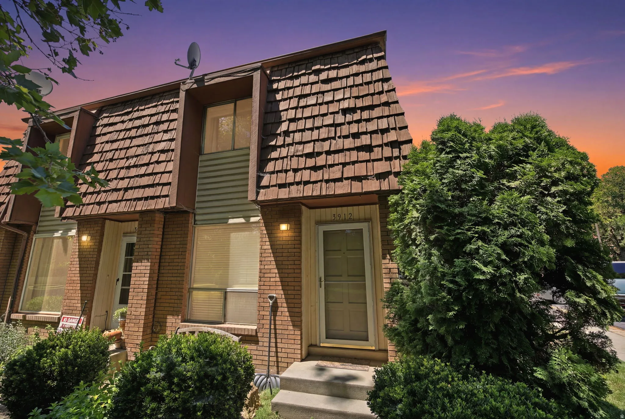 Townhome exterior featuring brick and siding facade, dimensional shingle roof, established evergreen landscaping, and front entry with steps