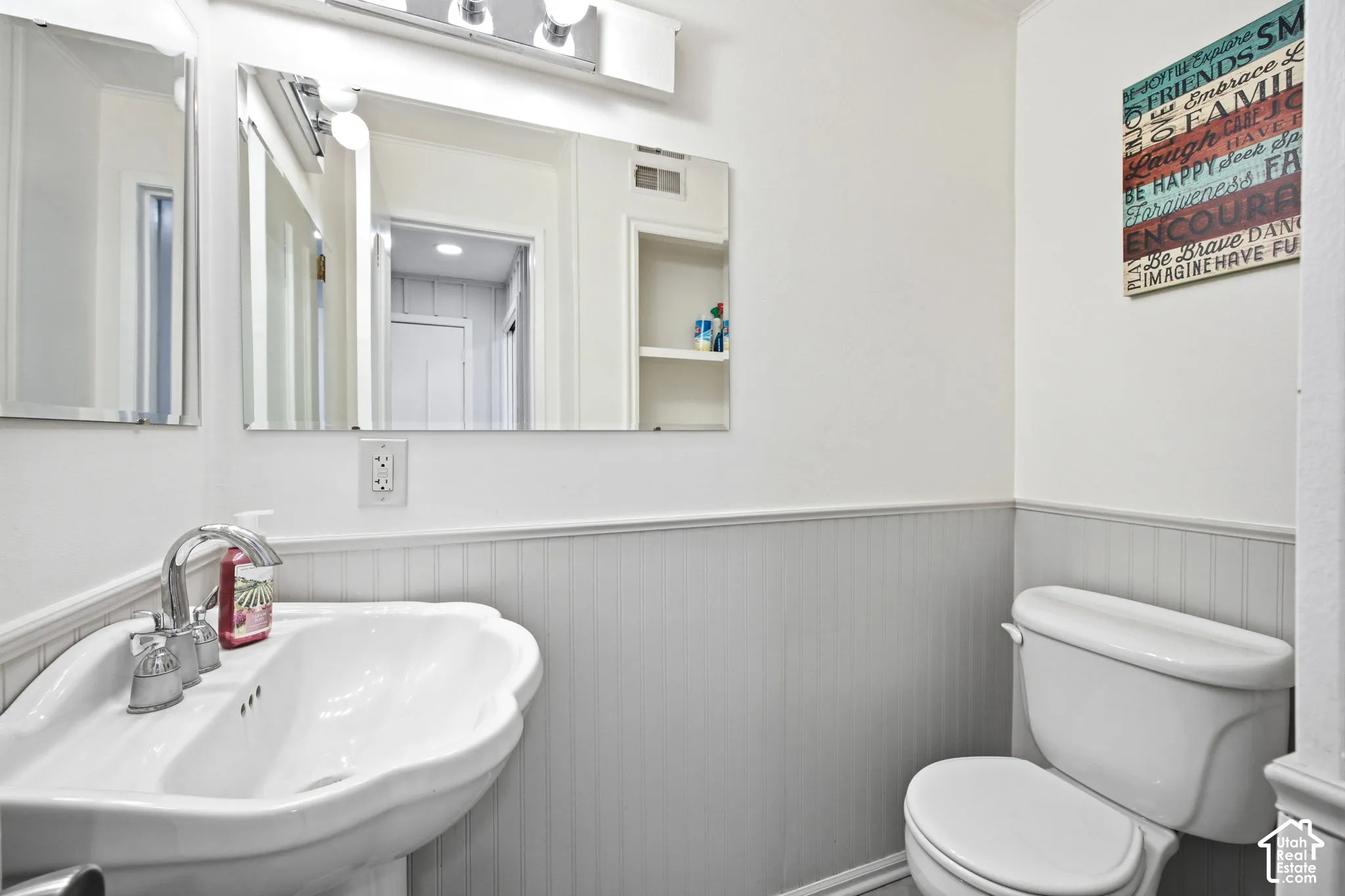 Bathroom featuring a pedestal sink with chrome faucet, a toilet, and beadboard wainscoting